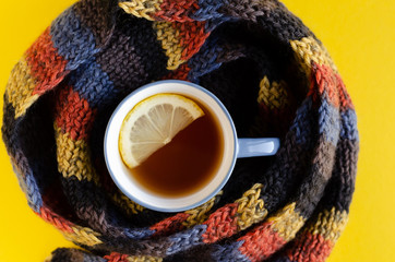 Woolen scarf with tea cup and lemon slice composition on yellow background.