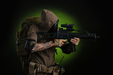man Stalker with a gun with a telescopic sight and a backpack in a gas mask on a dark background...