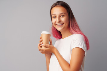 Nice teenager girl holding a cup of coffee over a gray background.