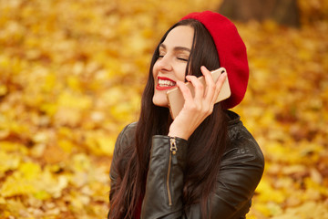 Outdoor shot of young happy Caucasian dark haired woman with smartphone, charming lady sitting on...
