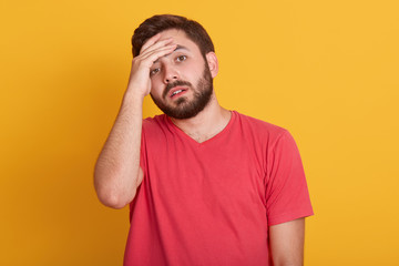 Studio shot of tensed bearded young man touches his forehead and having headache, wearing red...