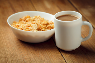 Crispy healthy dry cereal flakes in deep white plate on wooden background with cup of coffee with milk