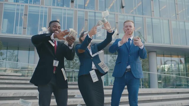 Diverse group of rich businessmen throw handful of banknotes in the air. Multiracial businessmen fooling around, throw cash in front of office building
