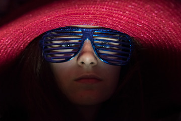 portrait d'une jeune fille avec des lunettes bleues et un chapeau rose