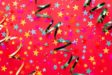 Festive red background with multicolor star shape confetti and streamers, copy space. Background...