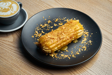 Appetizing and large eclair with glaze of mango on top and fir cream inside on a black plate....