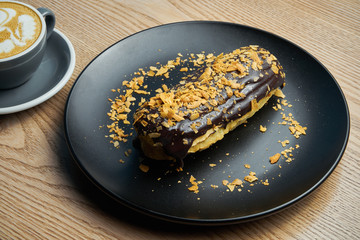 Appetizing and large eclair with glaze of chocolate on top and fir cream inside on a black plate. Sweets and dessert for coffee and tea.