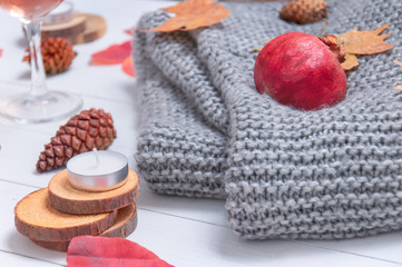 Fototapeta na wymiar Small candles, two glasses with rose wine, cones, dry red leaves, a gray scarf knitted on a white wooden table. Hello, Autumn. Cozy autumn background.