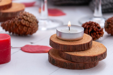 Small burning candles, two glasses with rose wine, cones, dry red leaves, a gray scarf knitted on a white wooden table. Hello, Autumn. Cozy autumn background.