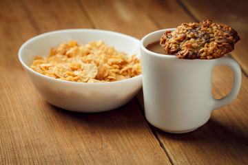 Crispy healthy dry cereal flakes in deep white plate on wooden background with cup of coffee with milk and homemade cookie