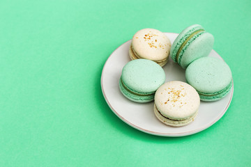 Delicious sweet dessert macaroons in white plate on mint paper background. France cookies with...