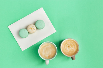 Cup coffee and tasty macaroons for breakfast on mint paper background. Cozy morning hot drinks and sweets for couple of people. Top view with copy space.