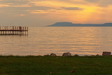 Pier with many birds at the Lake Balaton during sunset. Sun reflected in the water, mountain at the...