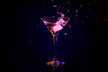 Dropping of ice cube into glass with tasty cocktail on dark background