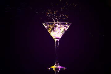 Dropping of ice cube into glass with tasty cocktail on dark background