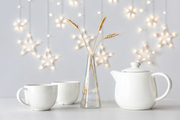 Teapot with cups and vase with wheat spikelets on table