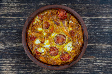 Ceramic bowl with vegetable frittata, simple vegetarian food. Frittata with tomato, pepper, onion and feta cheese on wooden table, close up. Italian egg omelette