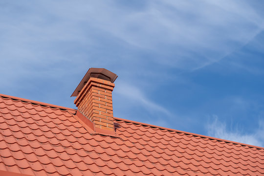 Red roof of a detached house and chimney against the blue sky, closeup