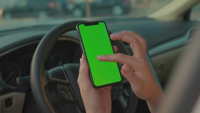 Female driver sitting in the car browsing online map on vertical mock-up smartphone greenscreen searching route planning a roadtrip. Lifestyle and technology.