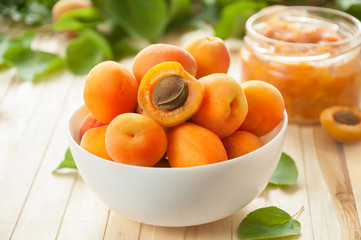 Ripe apricots with leaves in a white ceramic bowl on a light table. Apricot jam.