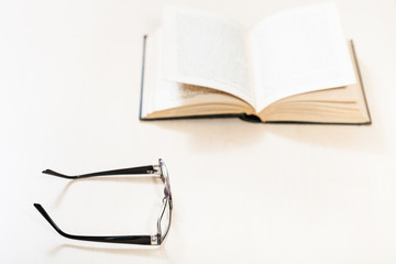 spectacles and open book on pale table