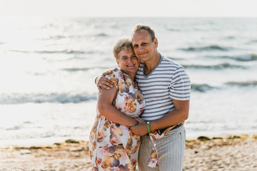 Romantic adult couple standing together on the beach. Mature pair relax at the seaside on holiday. Happy familiy walking and holding hands near sea. Husband embracing wife. Love story near the sea