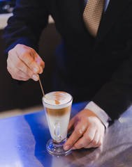 Barista using maker is using latte art in hot coffee.