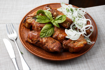 Grilled pork ribs in brown clay bowl close-up. Front view of plate with grilled pork ribs with onion and basil. Grey background. horizontal photo. Top view