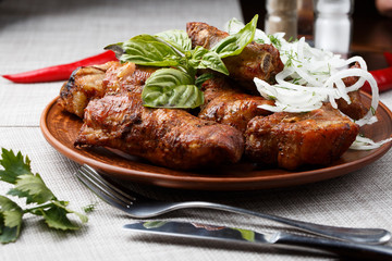 Grilled pork ribs in brown clay bowl close-up. Front view of plate with grilled pork ribs with onion and basil. Grey background. horizontal photo. Top view