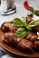 Grilled pork ribs in brown clay bowl close-up. Front view of plate with grilled pork ribs with onion and basil. Grey background. vertical photo. Top view
