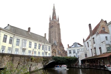 Fototapeta na wymiar canal and bridge of Bruges city in autumn, brick tower of the Church Of Our Lady or Onze-Lieve-Vrouwekerk in Bruges (Brugge), Belgium