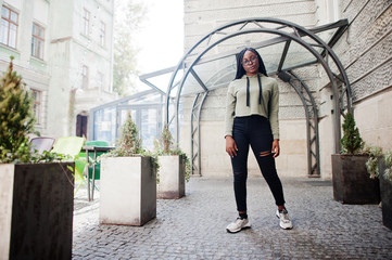 City portrait of positive young dark skinned female wearing green hoody and eyeglasses.