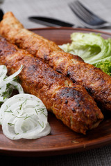 Shish kebab from ground beef meat. Lula kebab with white onion and salade, traditional Caucasian dish. Lined on a beautiful clay plate. vertical photo. grey background. top view.