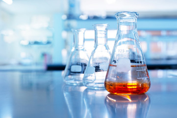 orange solution in science glass flask in blue chemistry school laboratory background - obrazy, fototapety, plakaty