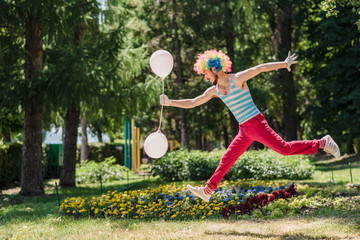 Mime jumps in the park with balloons. Clown in the air shows pantomime on the street.