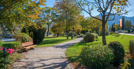 herbstlicher Kurpark Rottach-Egern am Tegernsee, Parkweg und Bank an einem sonnigen Herbsttag