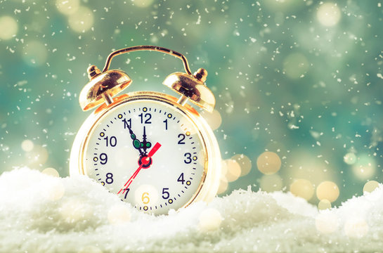 Christmas or New Year background with Golden alarm clock in snowdrifts on blue background with holiday lights counting last moments before Christmass Countdown to midnight.