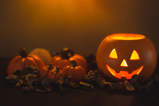 Halloween pumpkin head Jack lantern next to several pumpkins on orange background