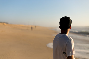 Jeune homme de dos sur une plage au coucher de soleil