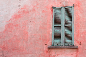 une vieille fenêtre verte et volets verts sur un mur rouge en italie