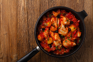 Traditionally prepared cod in Spanish. Served in tomato sauce with boiled potatoes, olivki and basil. Top view.