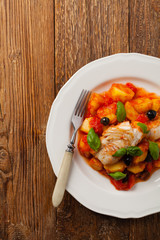 Traditionally prepared cod in Spanish. Served in tomato sauce with boiled potatoes, olivki and basil. Top view.