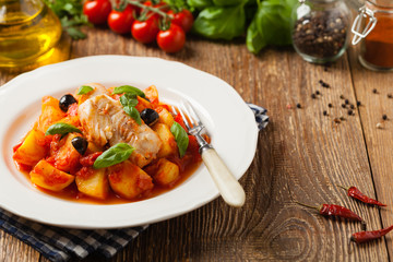 Traditionally prepared cod in Spanish. Served in tomato sauce with boiled potatoes, olivki and basil. Front view.
