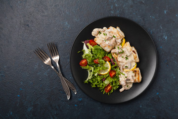 Fried cod served with mushroom sauce and salads. Portion on a black plate. Dark background.