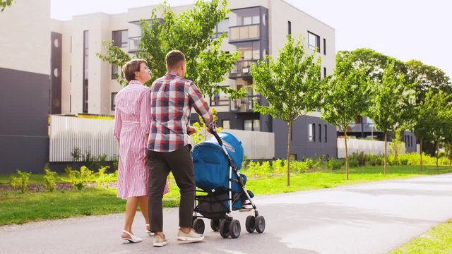 family, leisure and people concept - happy mother and father with little son in stroller walking along city street