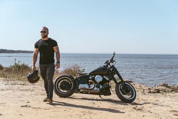 Handsome fit man holding helmet standing next to his bike