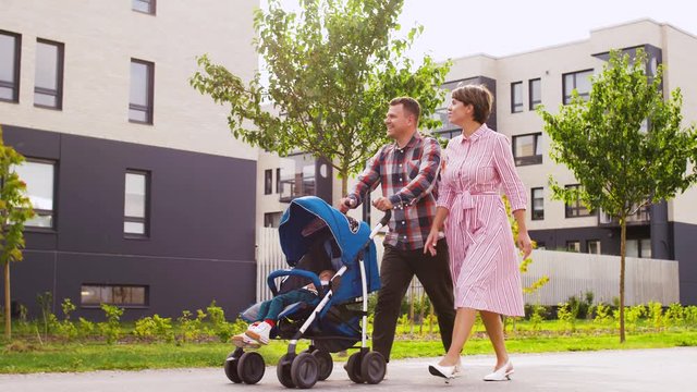 family, leisure and people concept - happy mother and father with little son in stroller walking along city street