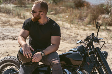 Sexy bearded biker sitting on his motorbike while posing