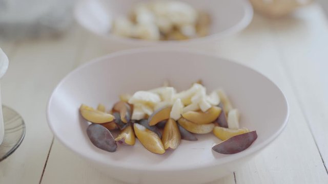 handheld camera. closeup of cutted fruits in pink bouls for fruit salad for healthy breakfast. top side view of white wooden table with ingredients for breakfast, dolly in, 4k