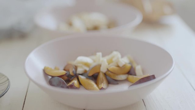 handheld camera. closeup of cutted fruits in pink bouls for fruit salad for healthy breakfast. top side view of white wooden table with ingredients for breakfast, dolly in, 4k